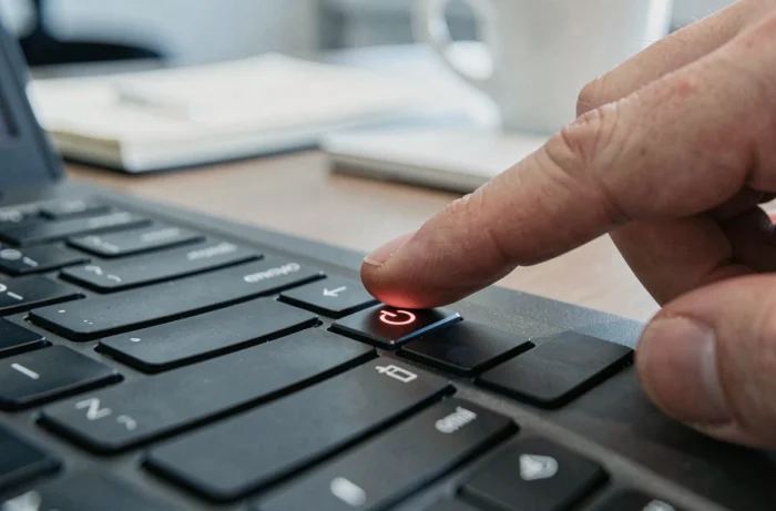 Gros plan sur le bouton power clignotant d'un laptop Lenovo avec une main sur le point de l'appuyer dans un bureau professionnel
